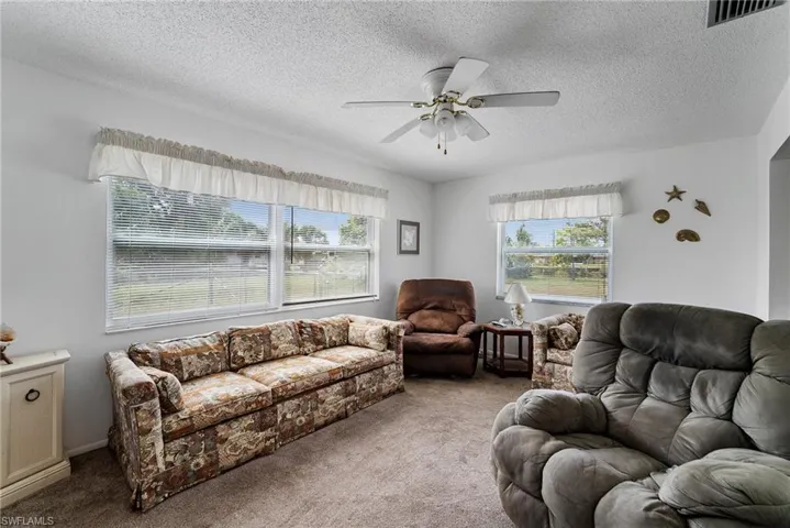 Living room featuring ceiling fan, carpet floors, and a textured ceiling