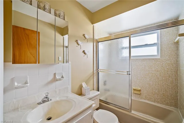 Full bathroom featuring tasteful backsplash, bath / shower combo with glass door, tile walls, toilet, and vanity