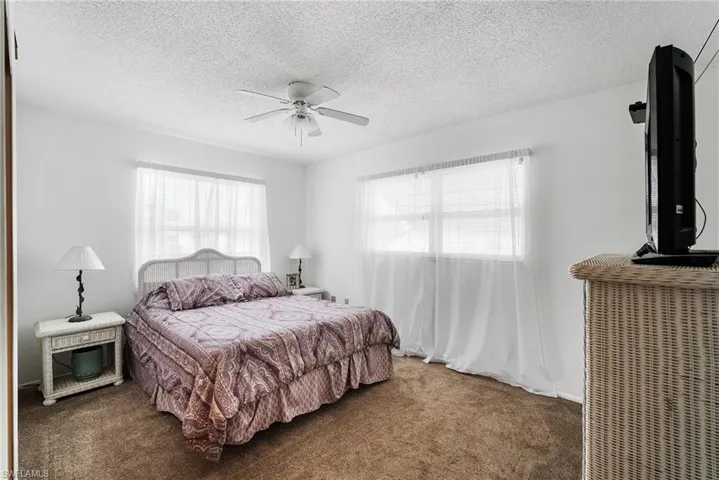Bedroom featuring ceiling fan, multiple windows, a textured ceiling, and dark colored carpet