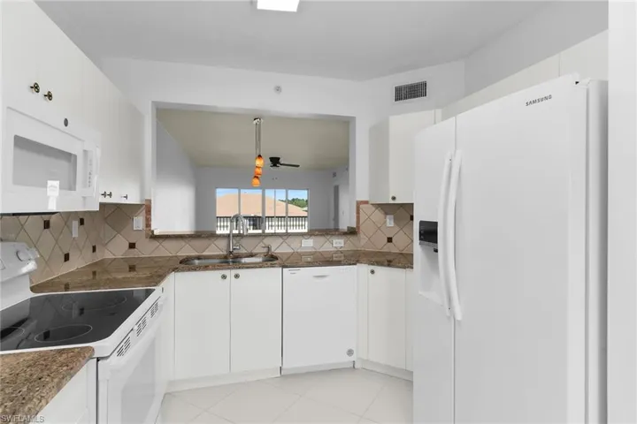 Kitchen with white appliances, white cabinets, backsplash, and dark stone countertops