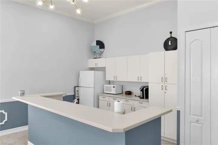 Kitchen with light countertops, white cabinets, crown molding, white appliances, and a center island