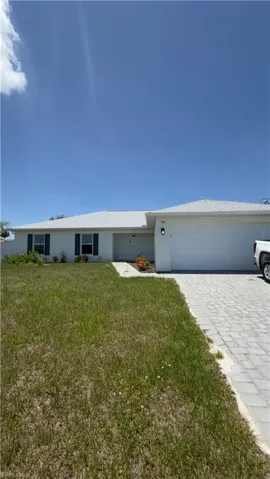 White stucco exterior featuring a gray shingle roof, blue window shutters, an attached garage, and a paver driveway