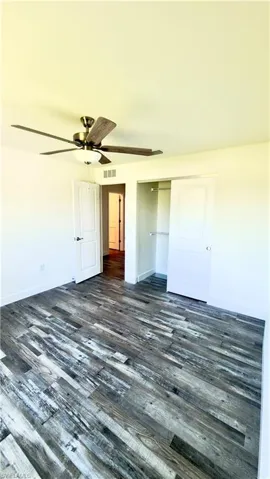 Spacious room featuring wood-finish flooring, a ceiling fan with integrated lighting, and a closet with sliding doors