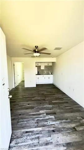 Spacious living area featuring wood-finish flooring, a ceiling fan with integrated lighting, and a neutral color palette