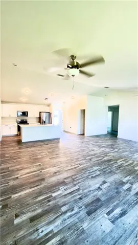 Open-concept living space featuring wood-finish flooring, a contemporary ceiling fan, recessed lighting, and a kitchen island with white cabinetry and stainless steel appliances