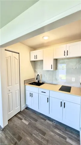 Compact kitchen space featuring white shaker cabinetry, an integrated black sink with a matte black faucet, a flush-mount cooktop, and light-toned countertops