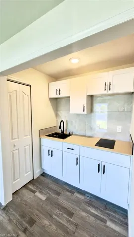 Compact kitchen area featuring white shaker-style cabinetry, a built-in cooktop, and a matte black faucet