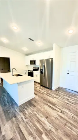 Open-concept kitchen featuring an island with an undermount sink, stainless steel appliances, white cabinetry, and wood-finish flooring