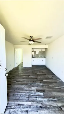 Open-concept living area featuring wood-finish flooring, a ceiling fan with integrated lighting, and a compact kitchen space
