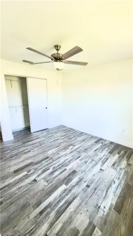 Spacious room featuring wide plank wood-finish flooring, a ceiling fan with integrated lighting, and a closet with sliding doors and built-in shelving