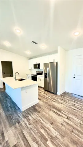 Modern kitchen featuring an island with an undermount sink and gooseneck faucet, white cabinetry, stainless steel appliances, and wood-finish flooring