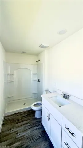 Bathroom featuring wood-finish flooring, a white shower stall with built-in shelving, a white vanity with cabinet storage, a white countertop, and recessed ceiling lighting