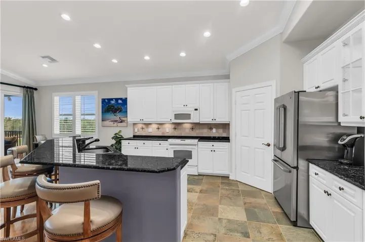 Kitchen with tasteful backsplash, white appliances, a kitchen island with sink, sink, and white cabinetry