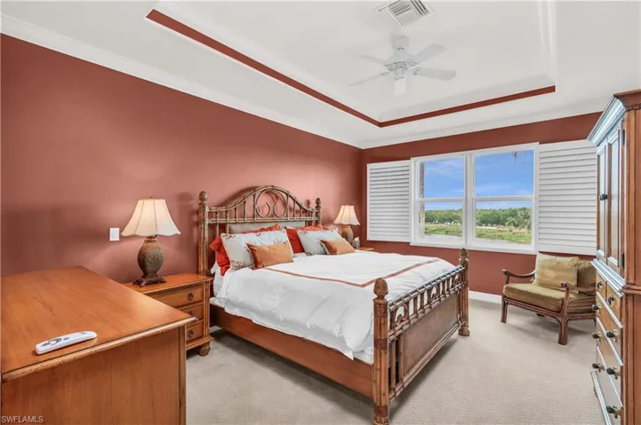 Bedroom featuring ceiling fan, ornamental molding, light carpet, and a tray ceiling