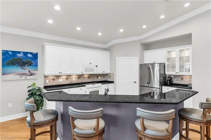 Kitchen with decorative backsplash, light wood-type flooring, white appliances, white cabinetry, and a breakfast bar area