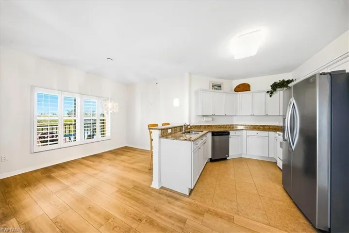 Kitchen with stainless steel appliances, a peninsula, white cabinets, dark stone countertops, and a chandelier