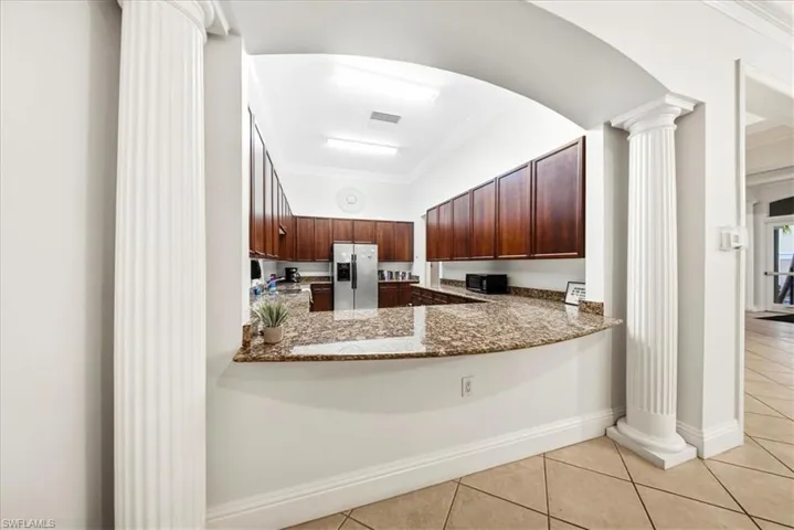 Kitchen featuring ornate columns, ornamental molding, stainless steel refrigerator with ice dispenser, light tile patterned floors, and black microwave