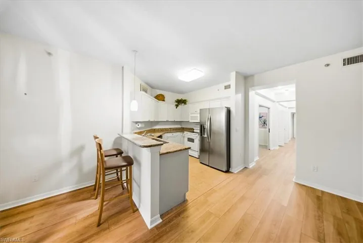 Kitchen with white appliances, hanging light fixtures, white cabinetry, a breakfast bar area, and light wood-style floors