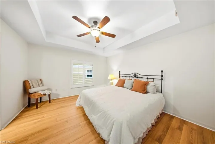 Bedroom with a tray ceiling, light wood-style floors, and a ceiling fan