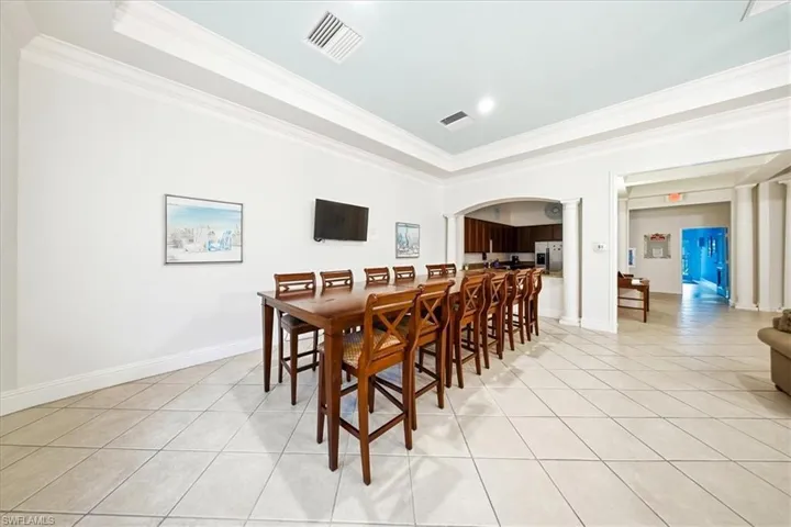 Dining space featuring light tile patterned flooring, a raised ceiling, crown molding, and arched walkways