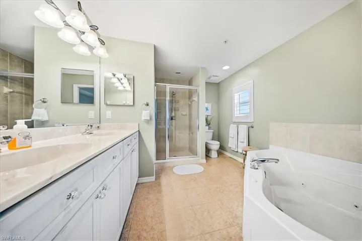 Full bath with double vanity, a whirlpool tub, a stall shower, and light tile patterned flooring