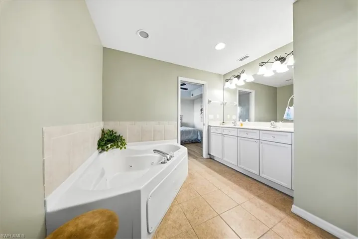 Full bathroom featuring connected bathroom, a jetted tub, double vanity, and light tile patterned flooring
