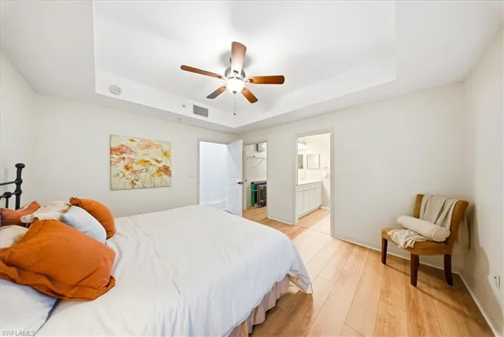 Bedroom featuring a tray ceiling, light wood-style flooring, ceiling fan, and ensuite bath