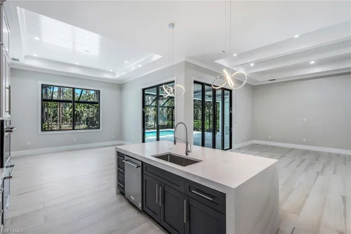Kitchen with decorative light fixtures, a raised ceiling, sink, a kitchen island with sink, and a chandelier