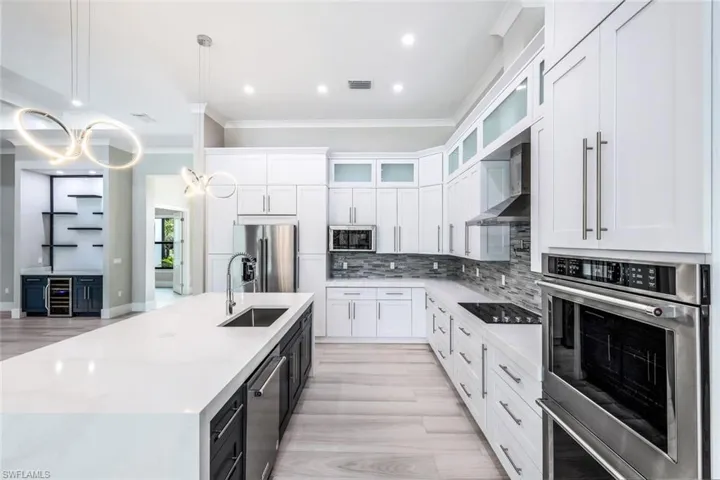 Kitchen featuring appliances with stainless steel finishes, a kitchen island with sink, wall chimney exhaust hood, pendant lighting, and sink
