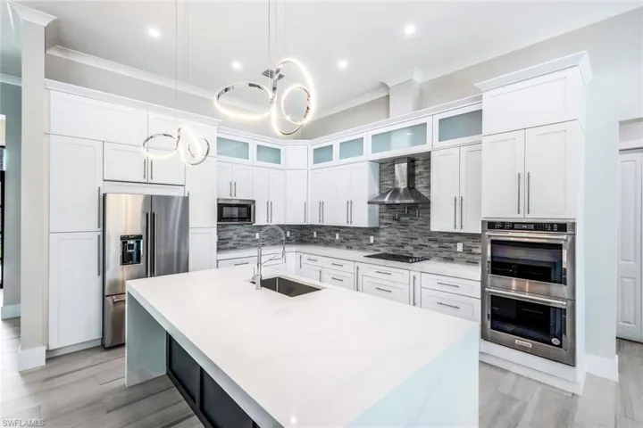 Kitchen with a center island with sink, appliances with stainless steel finishes, decorative light fixtures, backsplash, and sink