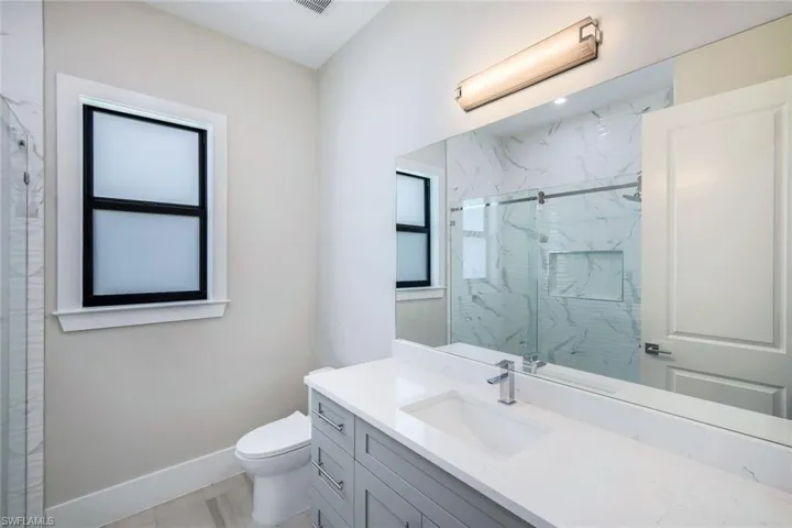 Bathroom with a shower with shower door, vanity, and toilet