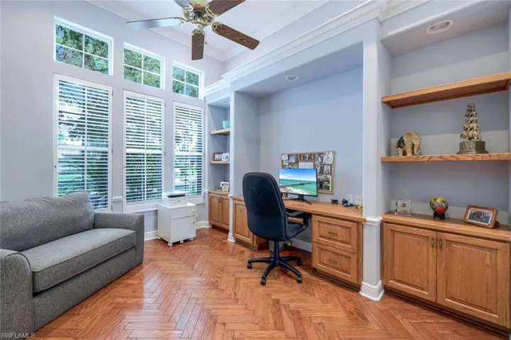 Home office with built in features, light parquet floors, plenty of natural light, and ceiling fan