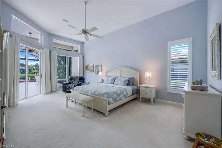 Carpeted bedroom with multiple windows, a towering ceiling, ceiling fan, and access to outside