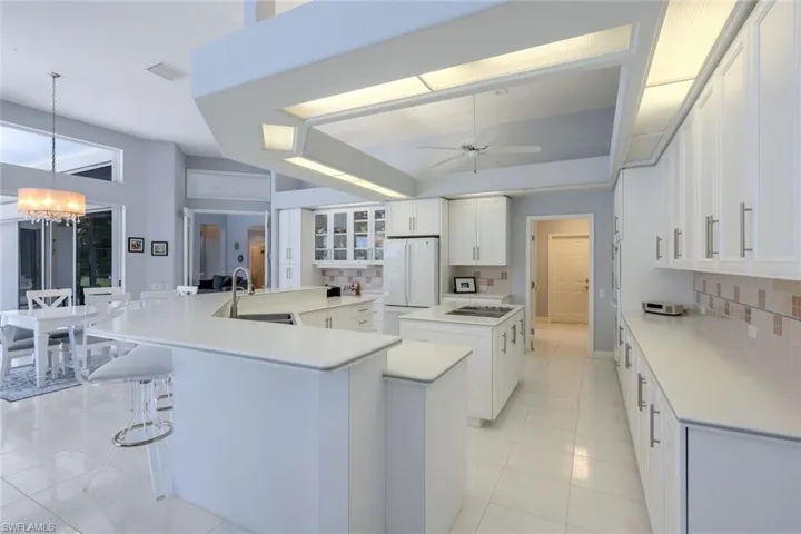 Kitchen featuring white refrigerator, ceiling fan with notable chandelier, a kitchen island with sink, sink, and tasteful backsplash