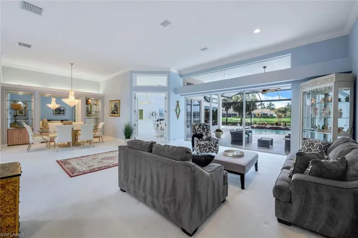 Living room with ornamental molding, carpet floors, and an inviting chandelier