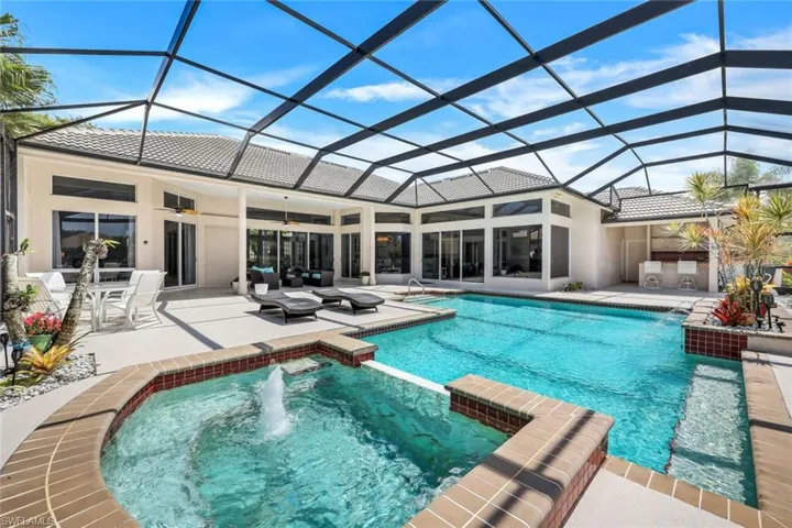 View of pool with glass enclosure, pool water feature, a patio area, and a hot tub
