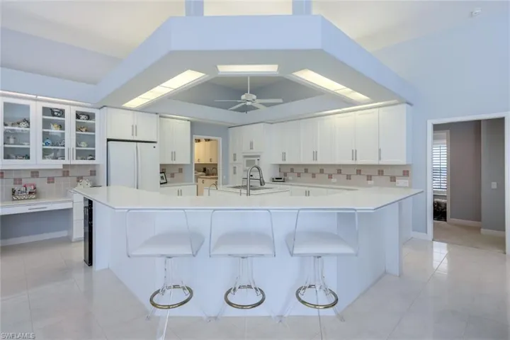 Kitchen featuring white refrigerator, white cabinets, ceiling fan, and a breakfast bar
