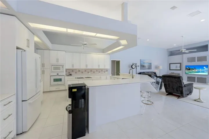 Kitchen with backsplash, ceiling fan, white cabinetry, and white appliances