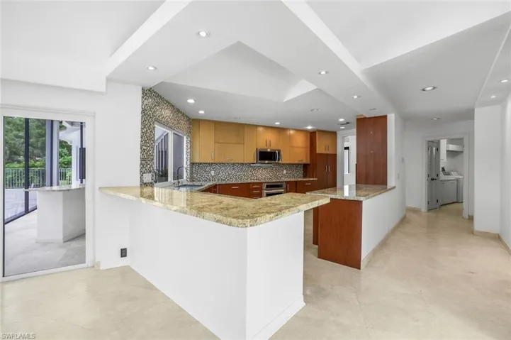 Kitchen with a peninsula, backsplash, light stone counters, brown cabinets, and stainless steel appliances