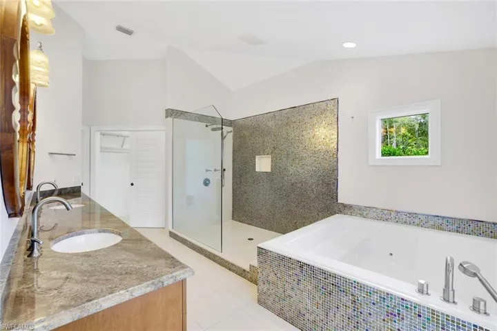 Full bathroom with a jetted tub, a walk in shower, double vanity, light tile patterned flooring, and vaulted ceiling