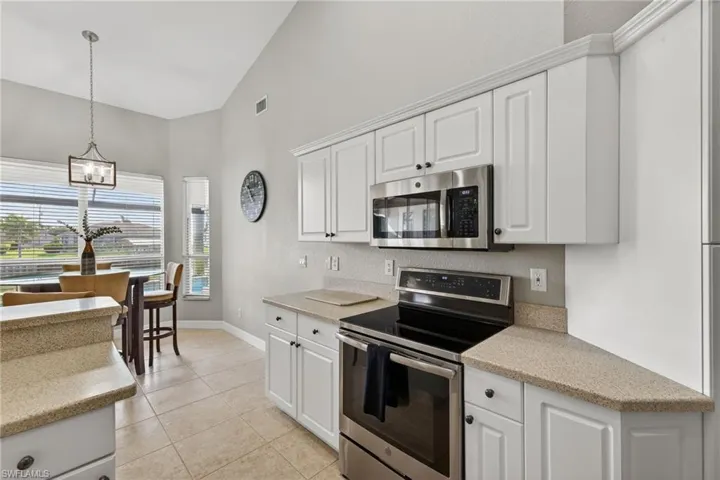 Kitchen with stainless steel appliances, white cabinets, light stone counters, vaulted ceiling, and hanging light fixtures
