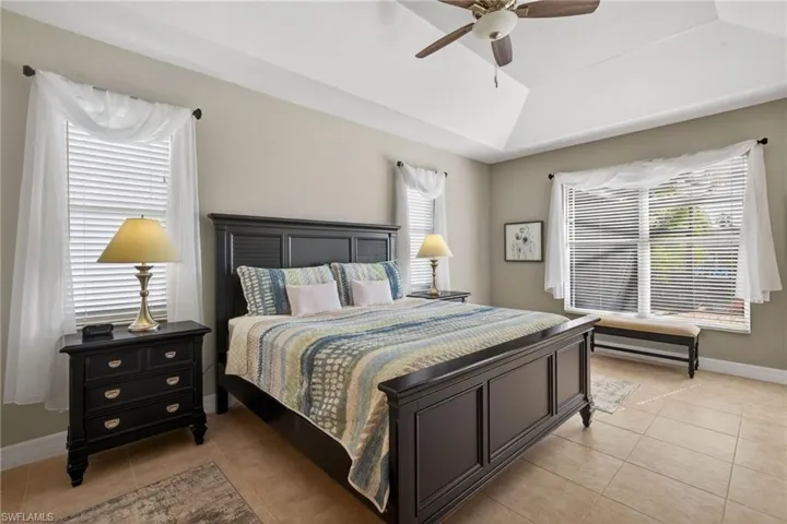 Bedroom with a raised ceiling, light tile patterned flooring, and a ceiling fan