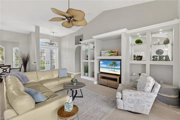 Tiled living area featuring built in shelves, french doors, arched walkways, vaulted ceiling, and a ceiling fan