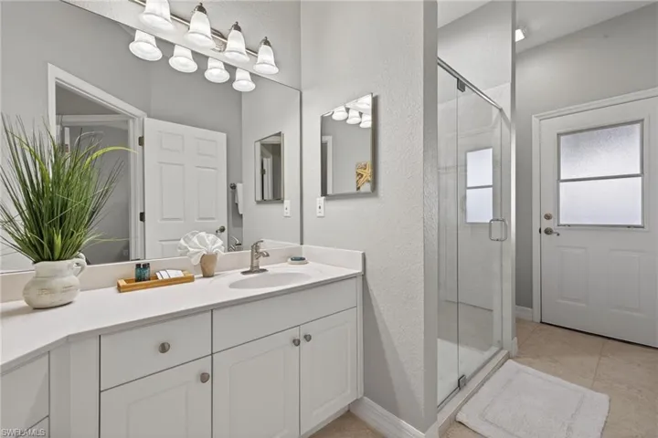 Bathroom featuring a shower stall, vanity, a textured wall, and light tile patterned floors