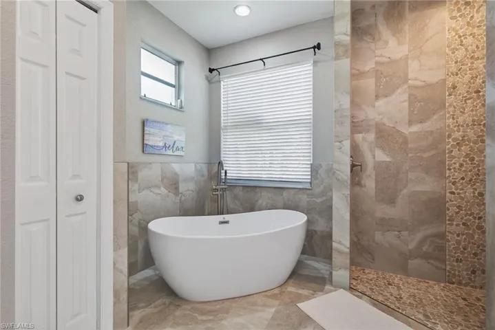 NEW Bathroom featuring tile walls, walk in shower, a freestanding tub, a closet, and wainscoting
