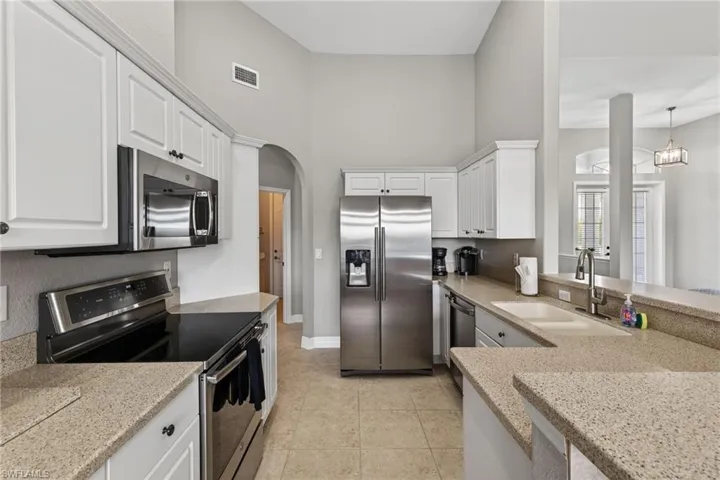 Kitchen featuring stainless steel appliances, arched walkways, white cabinets, light stone countertops, and a high ceiling
