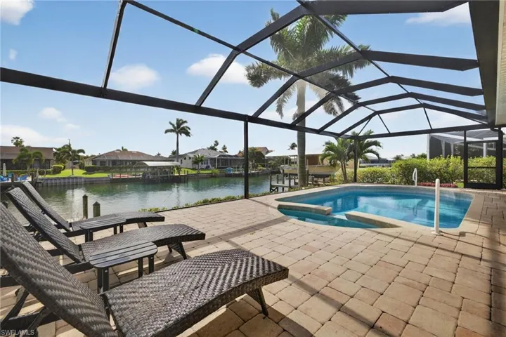 Outdoor pool featuring a sunroom, a patio, a water view, a lanai, and an in-ground hot tub