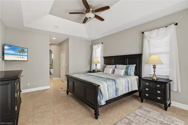 Bedroom featuring arched walkways, a ceiling fan, multiple windows, ensuite bath, and a tray ceiling