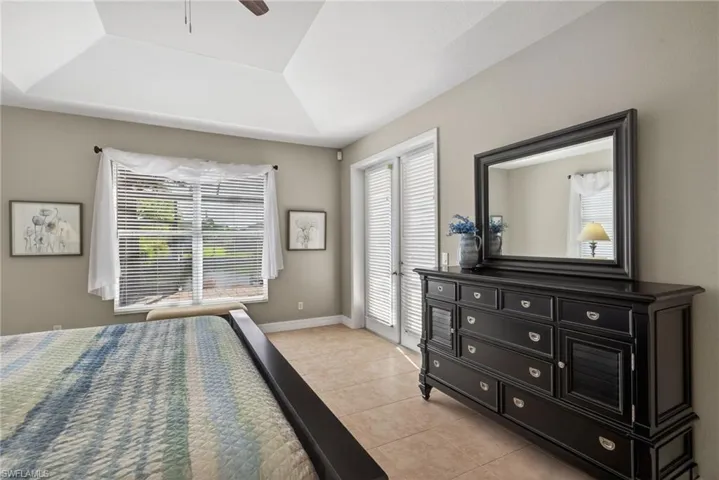Bedroom with a tray ceiling, light tile floors, a ceiling fan, and access to exterior