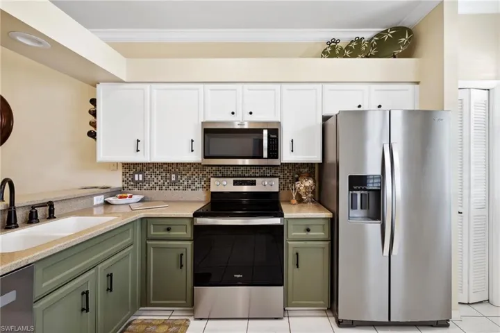 Kitchen with a sink, white cabinetry, green cabinetry, and stainless steel appliances